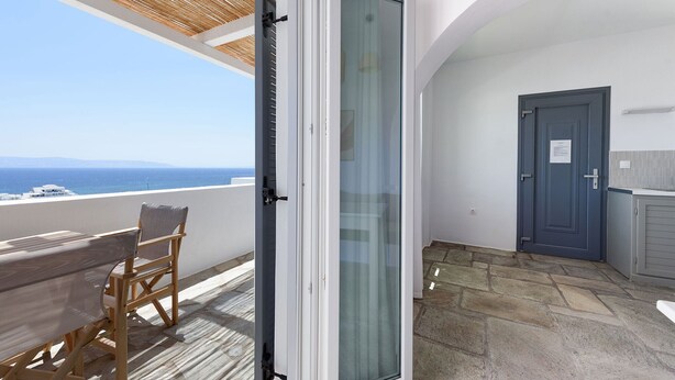 Un balcón con vista al mar, una puerta y un pequeño rincón de estar.