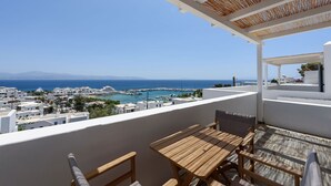 Un balcón con mesa y sillas de madera, con vista a un pueblo costero de edificios blancos y un puerto deportivo.