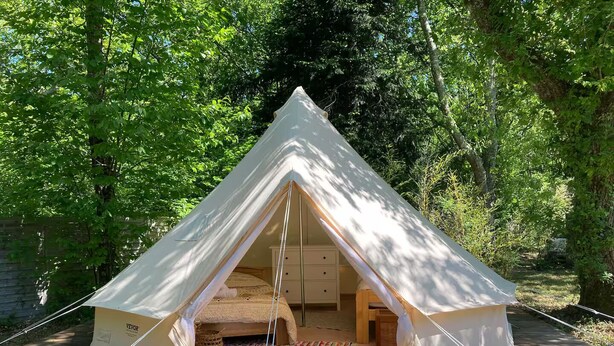 A white tent with a triangular entrance, set on a wooden deck surrounded by trees. - Evasion Nature Home & Glamping (Grayan-et-l'Hôpital)