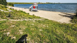 Ranta, jossa on pieni rakennelma, hiekkainen polku ja vesialue.