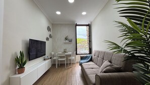 A modern living room with a sofa, TV, dining table, chairs, and a potted plant. - VV LAS ARENAS Renovated Apartment in Puerto de la Cruz (Puerto de la Cruz)