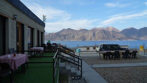An outdoor seating area with tables and chairs, a staircase, and a view of mountains and a body of water. - Mystic Pangong (Leh)