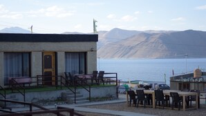 A building with a small outdoor seating area and a view of a body of water and mountains. - Mystic Pangong (Leh)