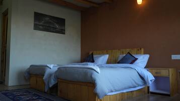 Un dormitorio con dos camas de madera, una mesita de noche, una lámpara de pared y un cuadro.