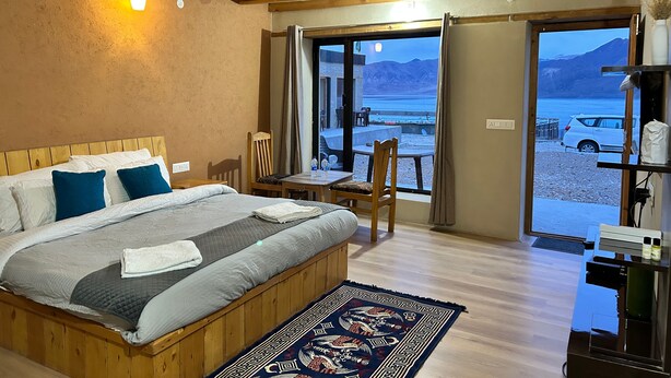 A bedroom with a large bed, wooden headboard, and a view of a lake and mountains through the door. - Mystic Pangong (Leh)