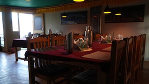 A dining area with wooden chairs and a red tablecloth. There are hanging lights and a painting on the wall. - Mystic Pangong (Leh)