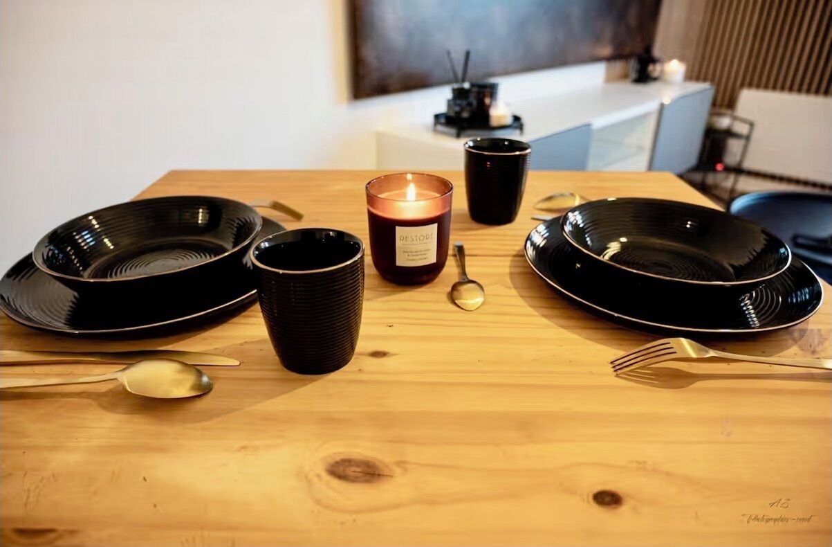 Ruokapöytä, jossa on mustat lautaset, kynttilä ja musta kynttilänjalka.