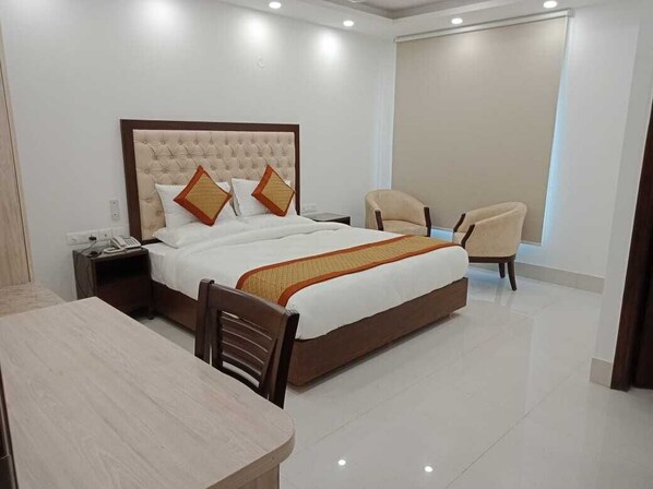 A hotel room with a large bed, a bedside table, a chair, and a desk. - Lemon Green Inn (New Delhi)