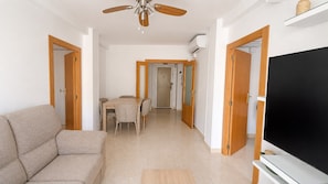 Una sala de estar con sofá, televisor, ventilador de techo y un comedor con sillas y mesa.