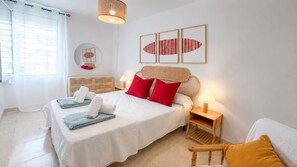 Habitación de hotel con cama, mesita de noche con lámpara, silla y una obra de arte en la pared.
