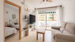 Una habitación de hotel moderna con cama, televisión, sofá, una mesita y un balcón con vistas a edificios.