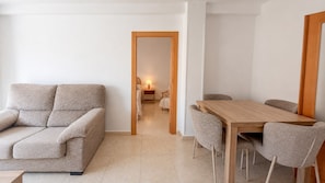 Una sala de estar con un sofá, una mesa de comedor con sillas y un pasillo que lleva a un dormitorio.