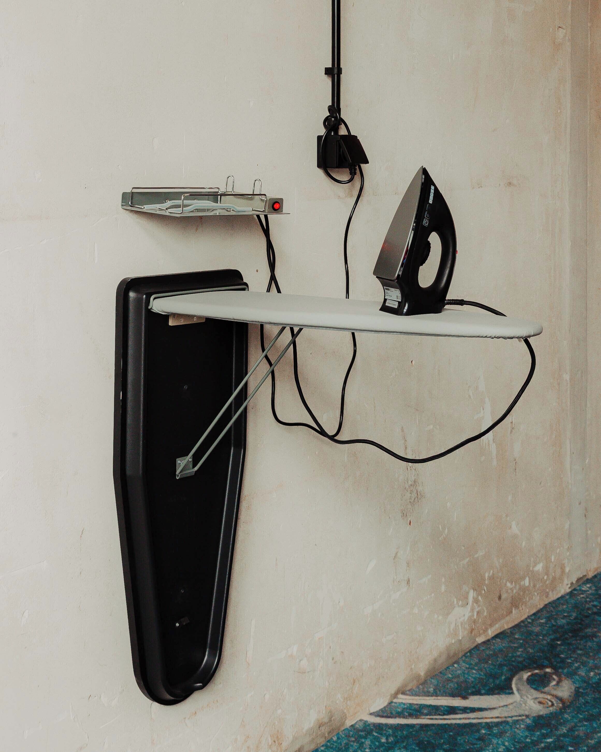 Eine an der Wand befestigte Büroeinrichtung mit Bügeleisen, Steckleiste und Kabel.
