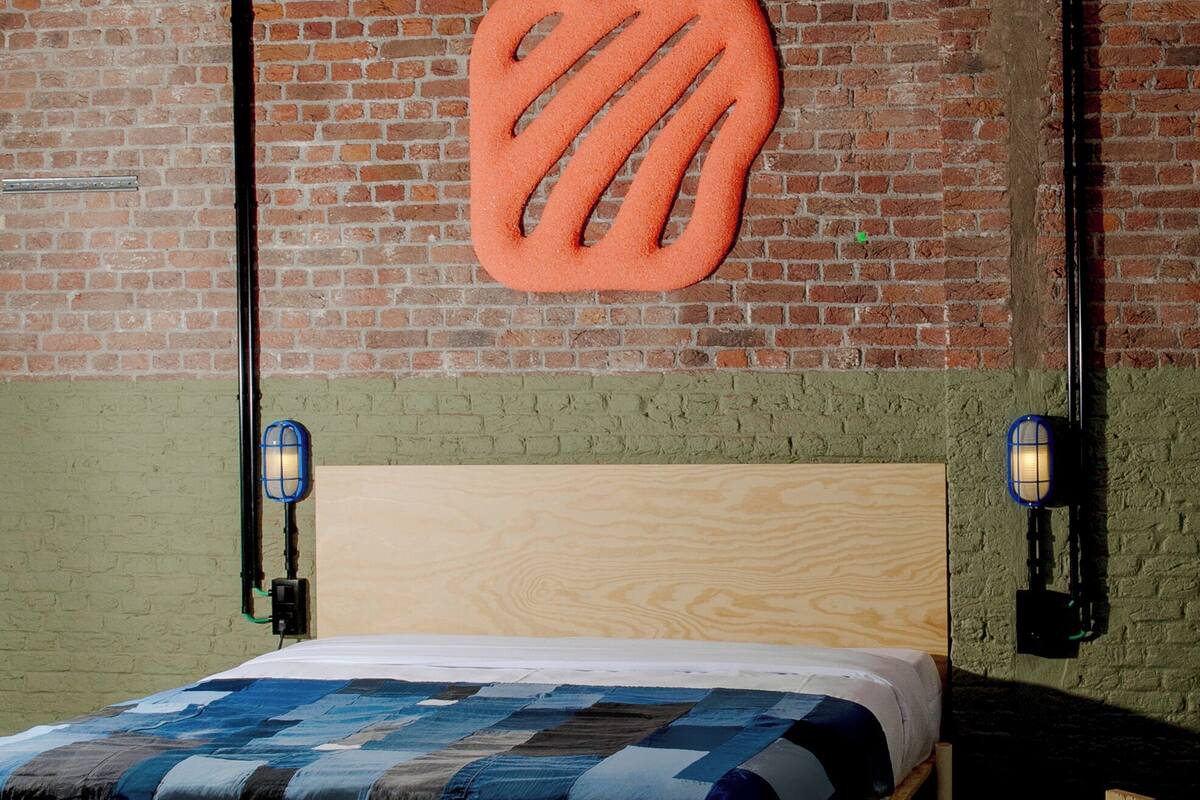 A room with a brick wall, a wooden bed with a blue and white quilt, and two wall-mounted lamps.