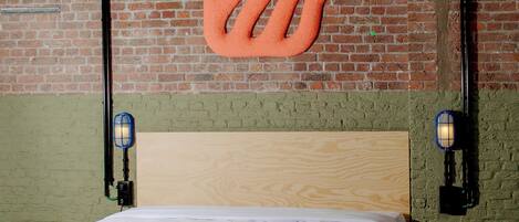 A room with a brick wall, a wooden bed with a blue and white quilt, and two wall-mounted lamps.