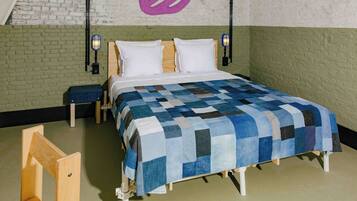 Un dormitorio con una cama de madera, una colcha azul y blanca a cuadros, dos mesitas de noche y una pared con un diseño abstracto morado.