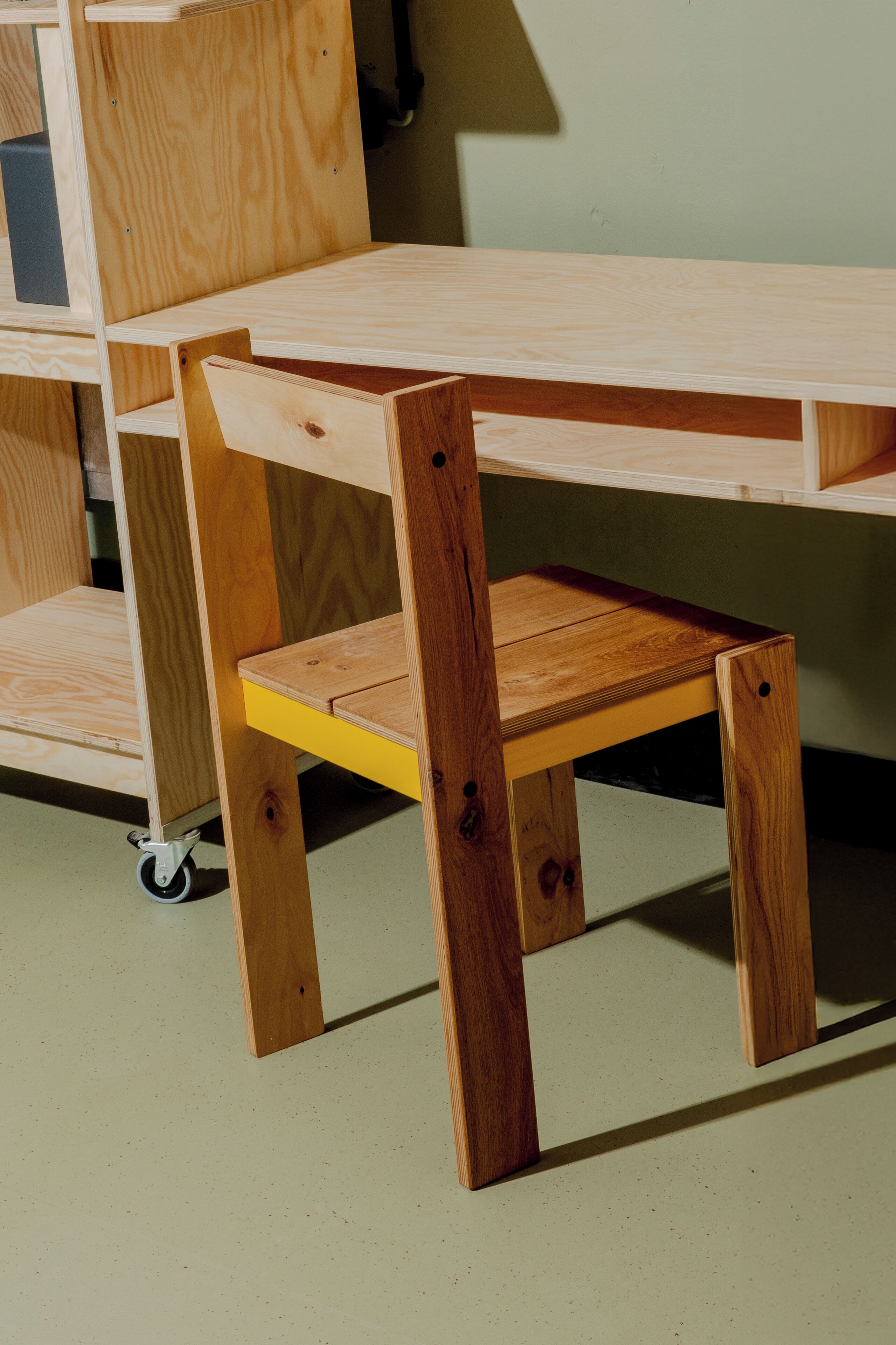 A wooden desk with a yellow shelf and a chair.