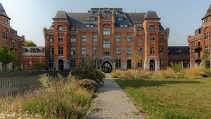 Un edificio grande y antiguo con un arco central, rodeado de un camino empedrado y zonas verdes.