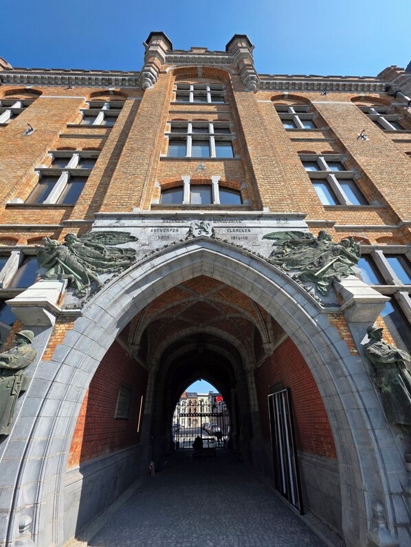 A large brick building with a prominent arched entrance, featuring statues and inscriptions.
