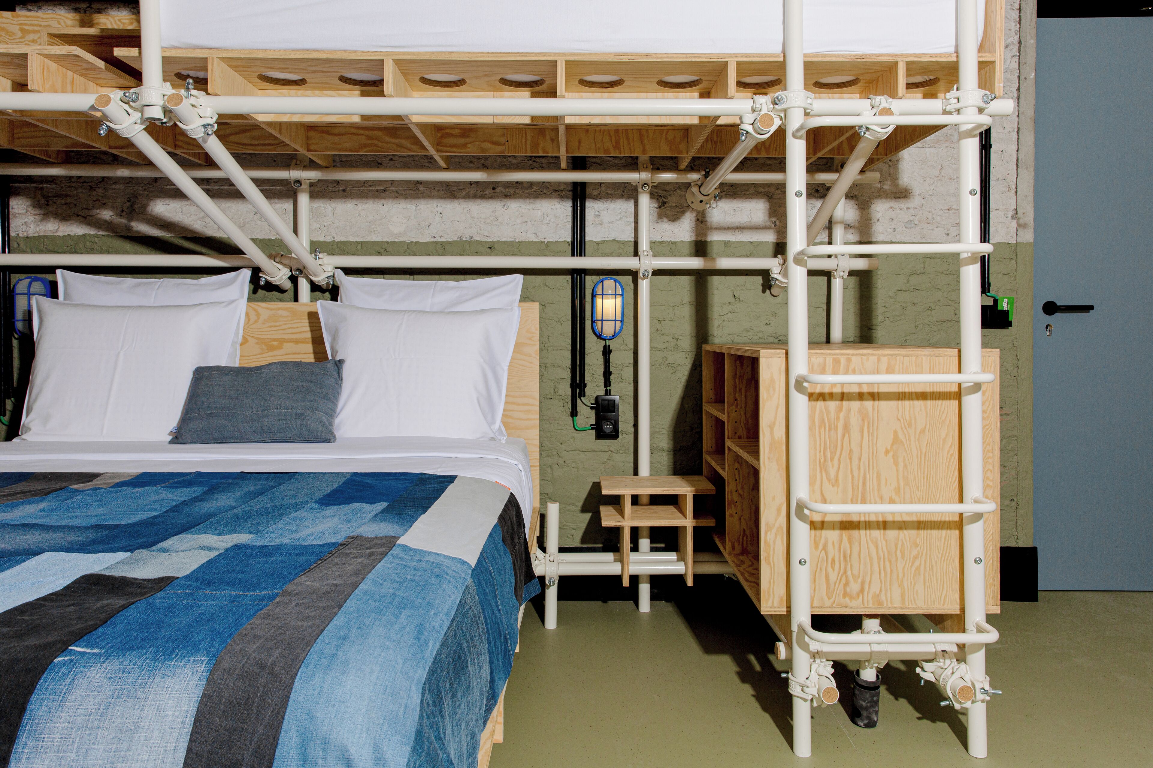 Un letto a castello con una scaletta in legno, un tavolino di legno e un faretto fissato al muro.