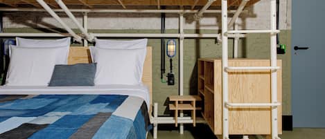 Una cama litera con escalera de madera, una mesita de madera y un aplique fijado a la pared.