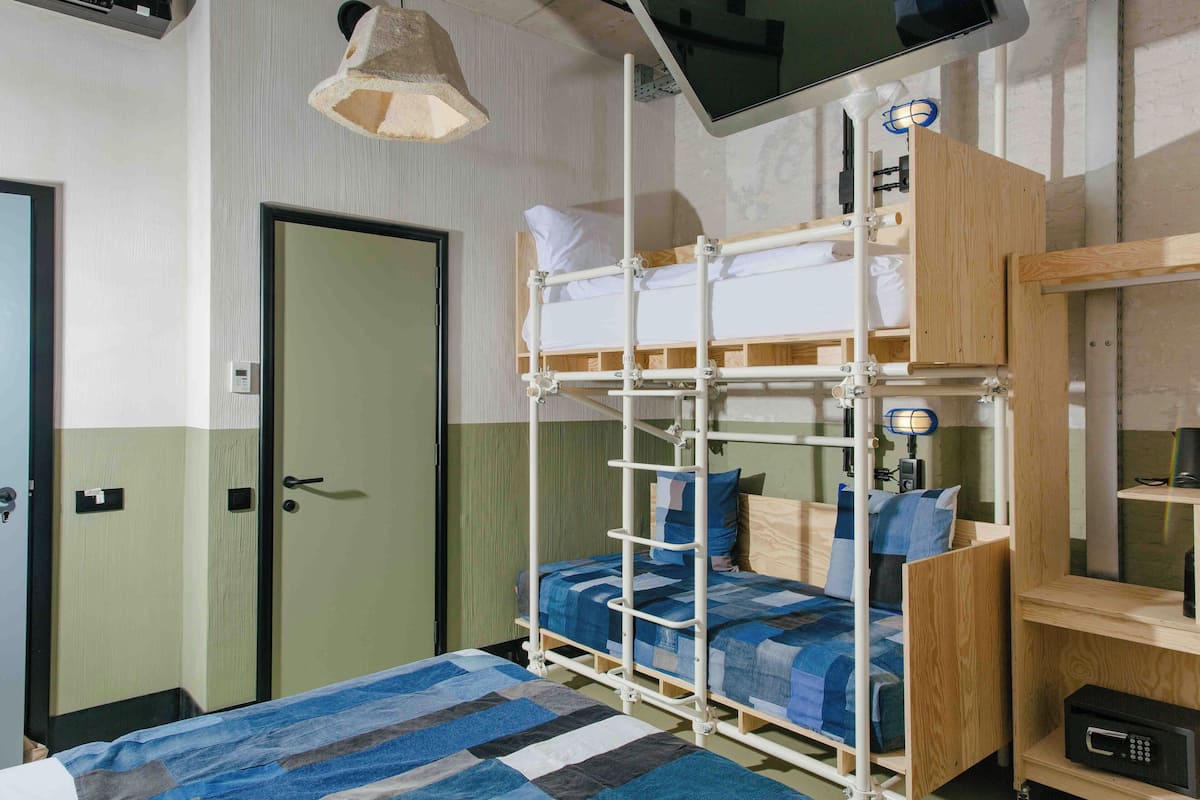 A bunk bed with a wooden frame, a bedside table, a lamp, and a television mounted on the wall.