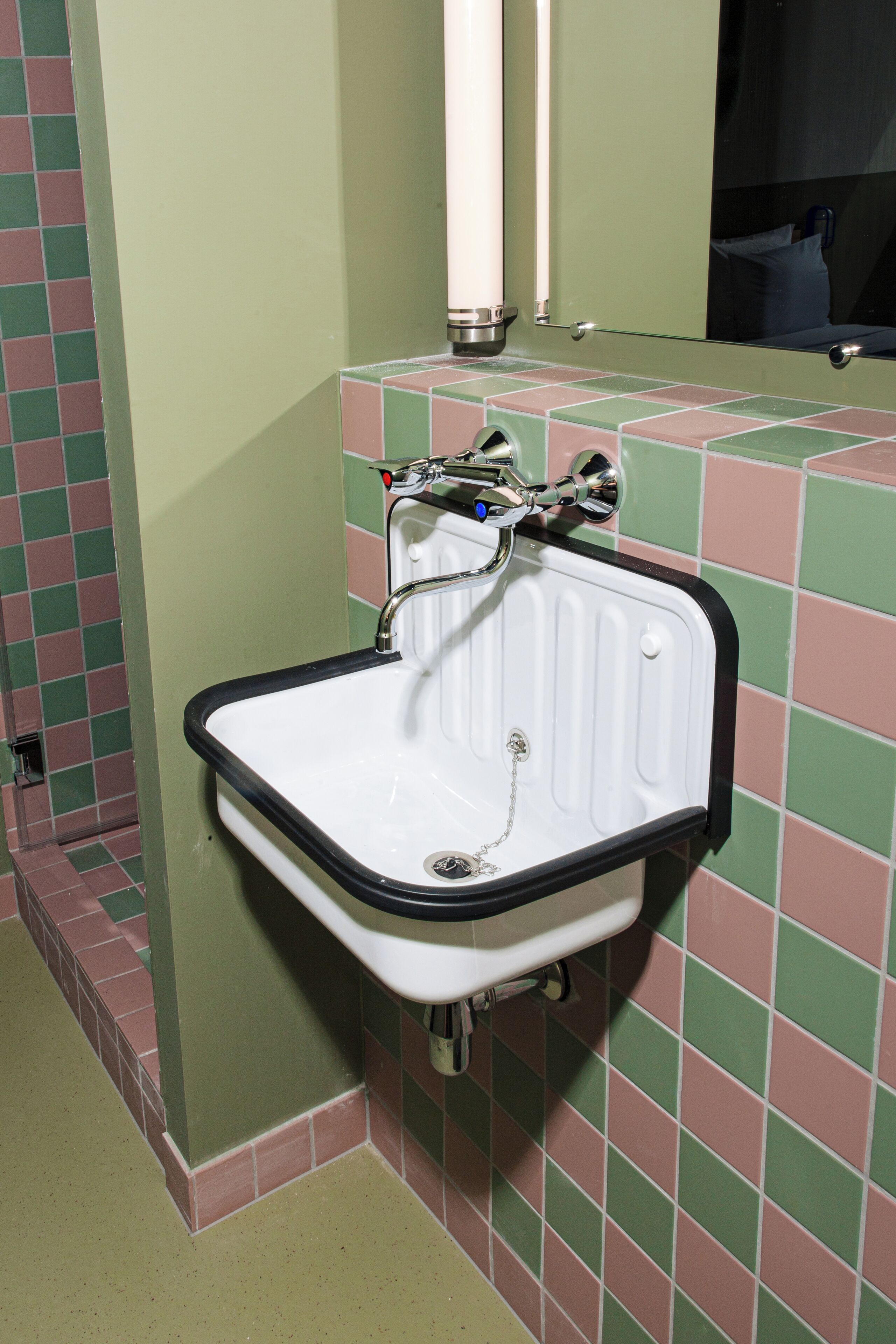 A bathroom with a white sink, green and pink tiled walls, and a mirror above the sink.