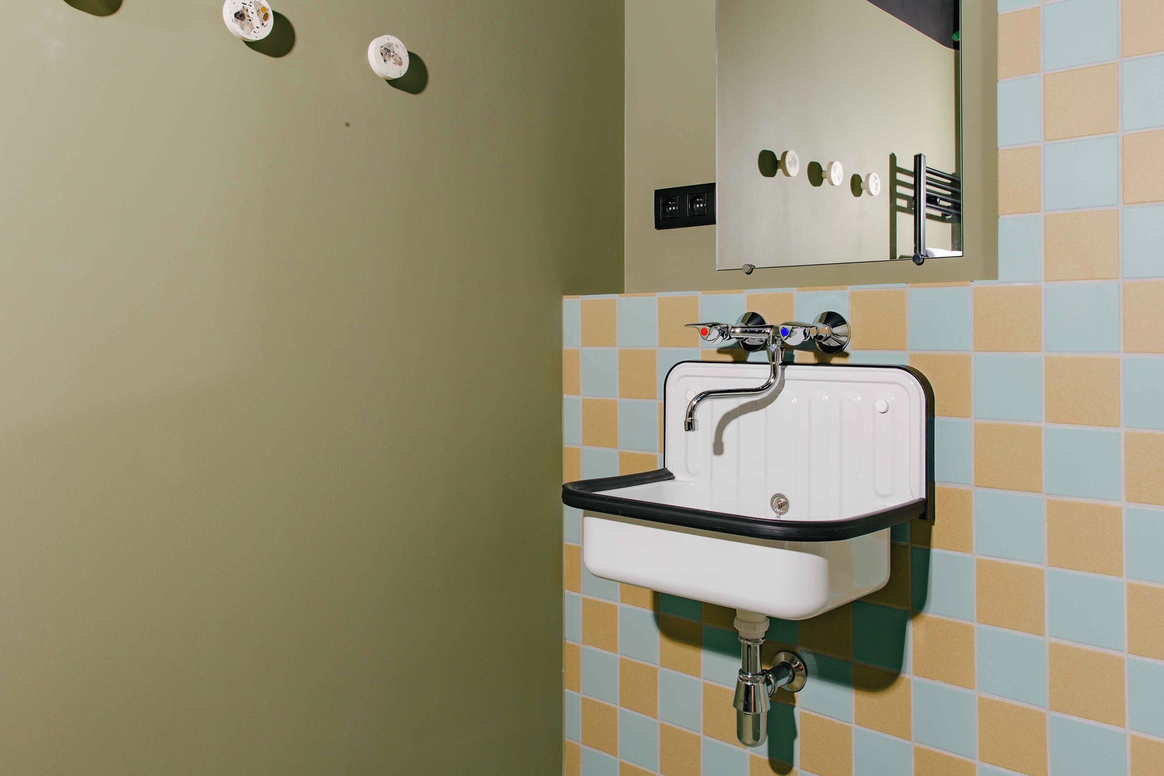 Une salle de bain avec un lavabo blanc, un miroir et un mur recouvert de carreaux.