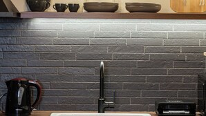 Een keuken met een witte spoelbak, een zwart metselwerk achterwand en een houten aanrecht.