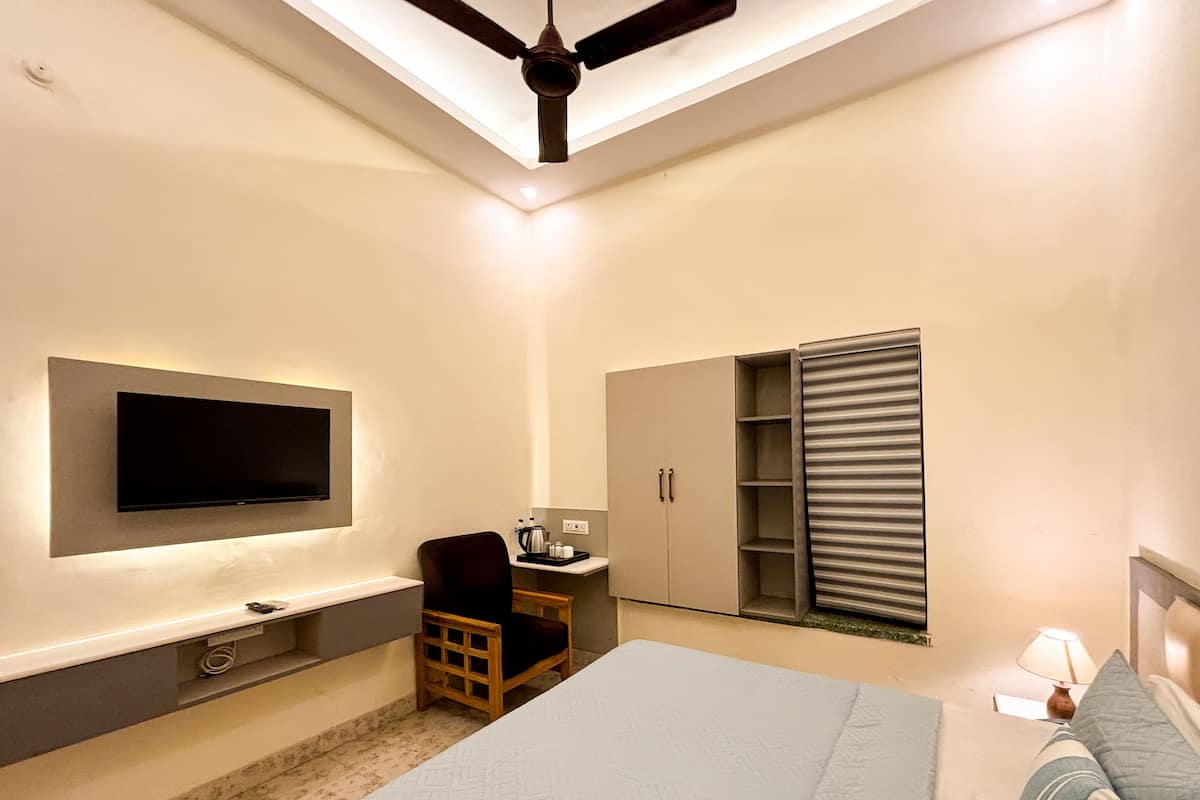 A modern bedroom with a flat-screen TV mounted on the wall, a bed with a headboard, a desk with a chair, a wardrobe, and a ceiling fan.