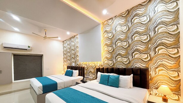 A hotel room with two beds, a large patterned wall, a ceiling fan, and an air conditioning unit. - Hotel Diamond Palace (Varanasi)