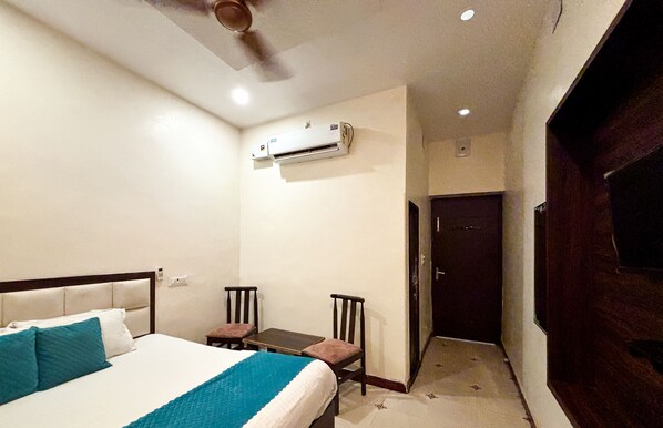 A hotel room with a bed, two chairs, a small table, an air conditioning unit, and a door leading to another room. - Hotel Diamond Palace (Varanasi)