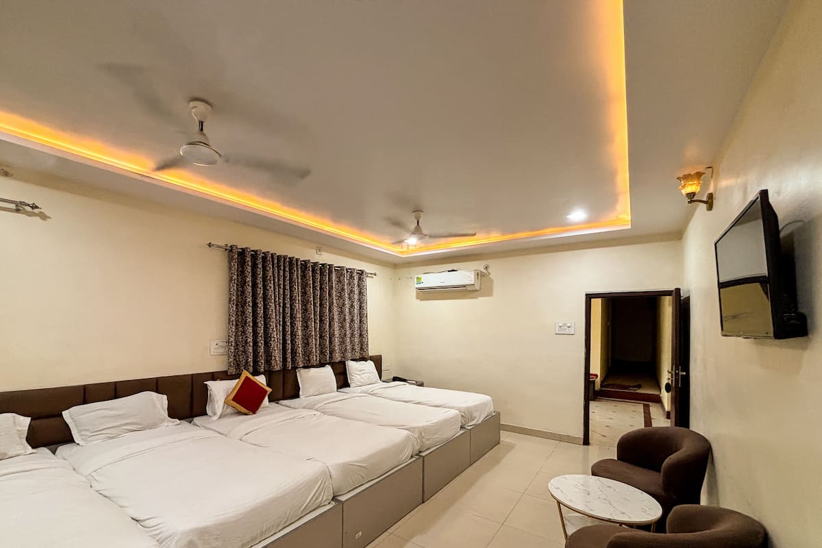 A hotel room with a large bed, a small table, a chair, a ceiling fan, an air conditioning unit, and a TV mounted on the wall.