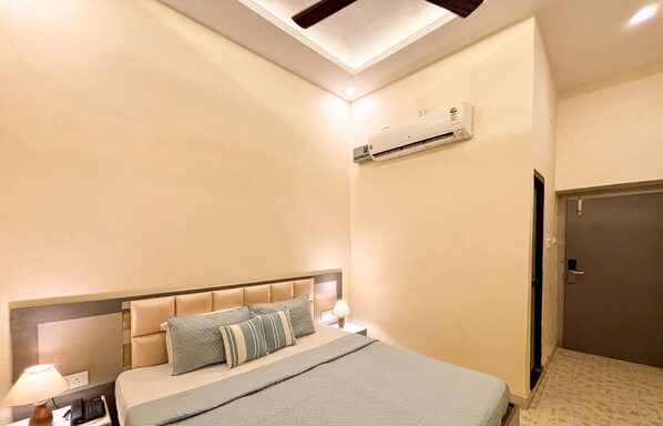 Une chambre d’hôtel équipée d’un lit, de lampes de chevet, d’un luminaire au plafond, d’un appareil de climatisation et d’une porte.