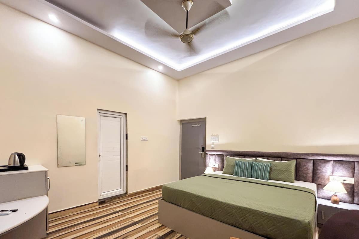 A hotel room with a bed, a bedside table, a chair, a small table, a mirror, and a door.