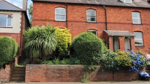 A two-story brick house with a front garden, a small window, and a visible chimney. - 157 Watling Street South (Church Stretton)