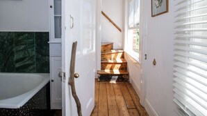 A narrow hallway with a wooden staircase leading to a second floor, a white door with a brass handle, and a window with blinds. - 157 Watling Street South (Church Stretton)