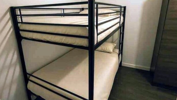 A bunk bed with a metal frame and beige bedding in a room with white walls and a wooden floor. - Park Road Retreat (Dudley)