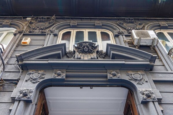 Une façade d’immeuble ornée de détails architecturaux raffinés, notamment un motif décoratif au-dessus de l’entrée et un appareil de climatisation sur le côté droit.