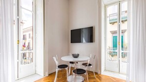 Comedor con una mesa redonda, cuatro sillas, un televisor de pantalla plana y vistas de edificios a través de un ventanal.