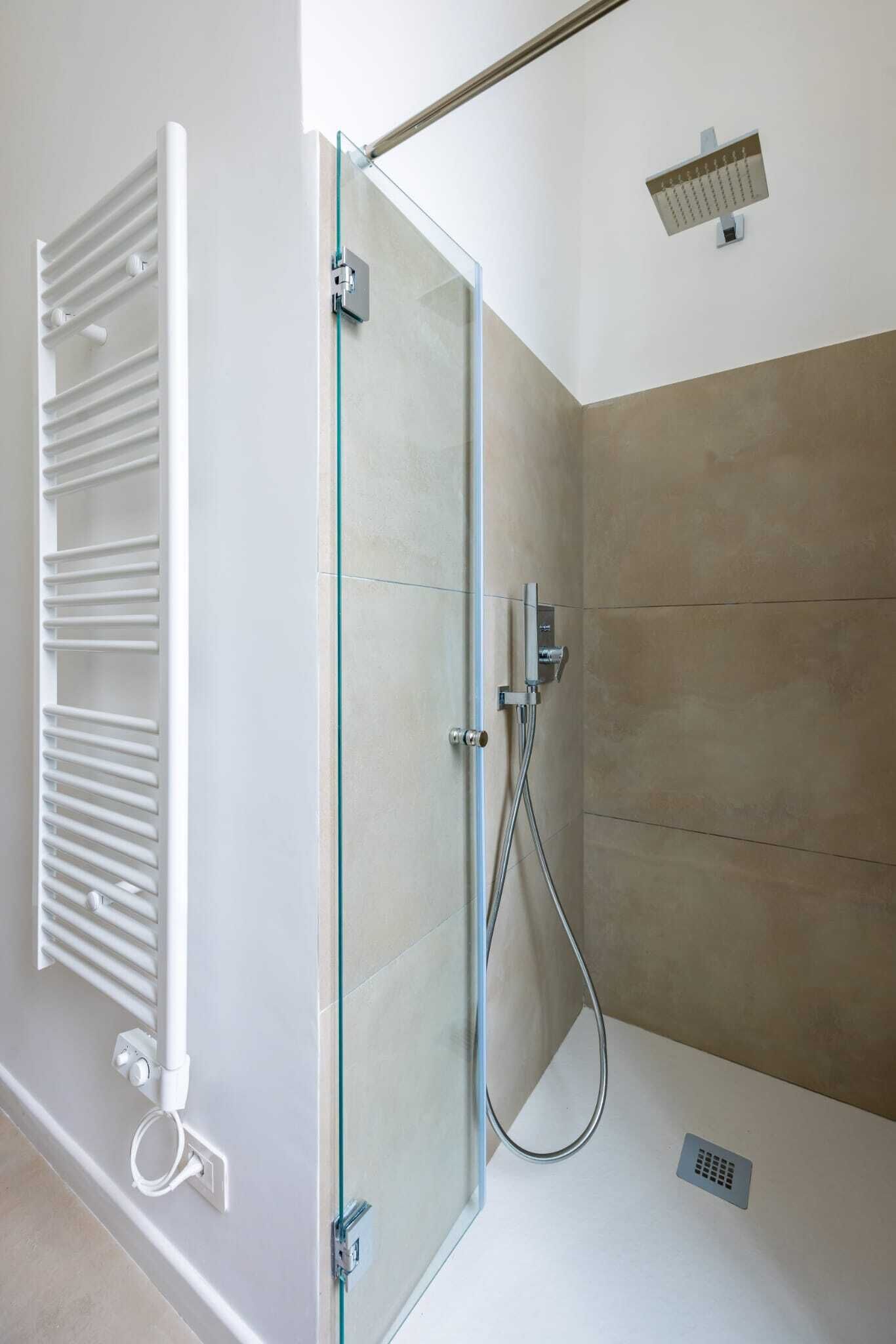 Ein moderner Duschbereich mit Glastür, weißem Handtuchhalter und einer an der Wand befestigten Bedienfeld.