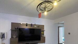 A modern living room with a large flat-screen TV mounted on a wooden wall unit, a patterned rug, and a unique ceiling light fixture.