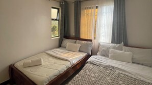 A bedroom with two beds, a window, and curtains.
