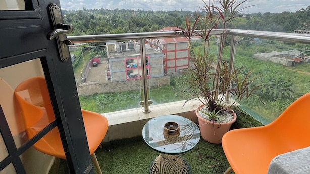 A balcony with artificial grass, two orange chairs, a small glass table, and potted plants.