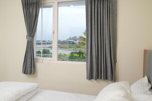 A room with a bed, a window with curtains, and a view of a bridge and greenery outside.