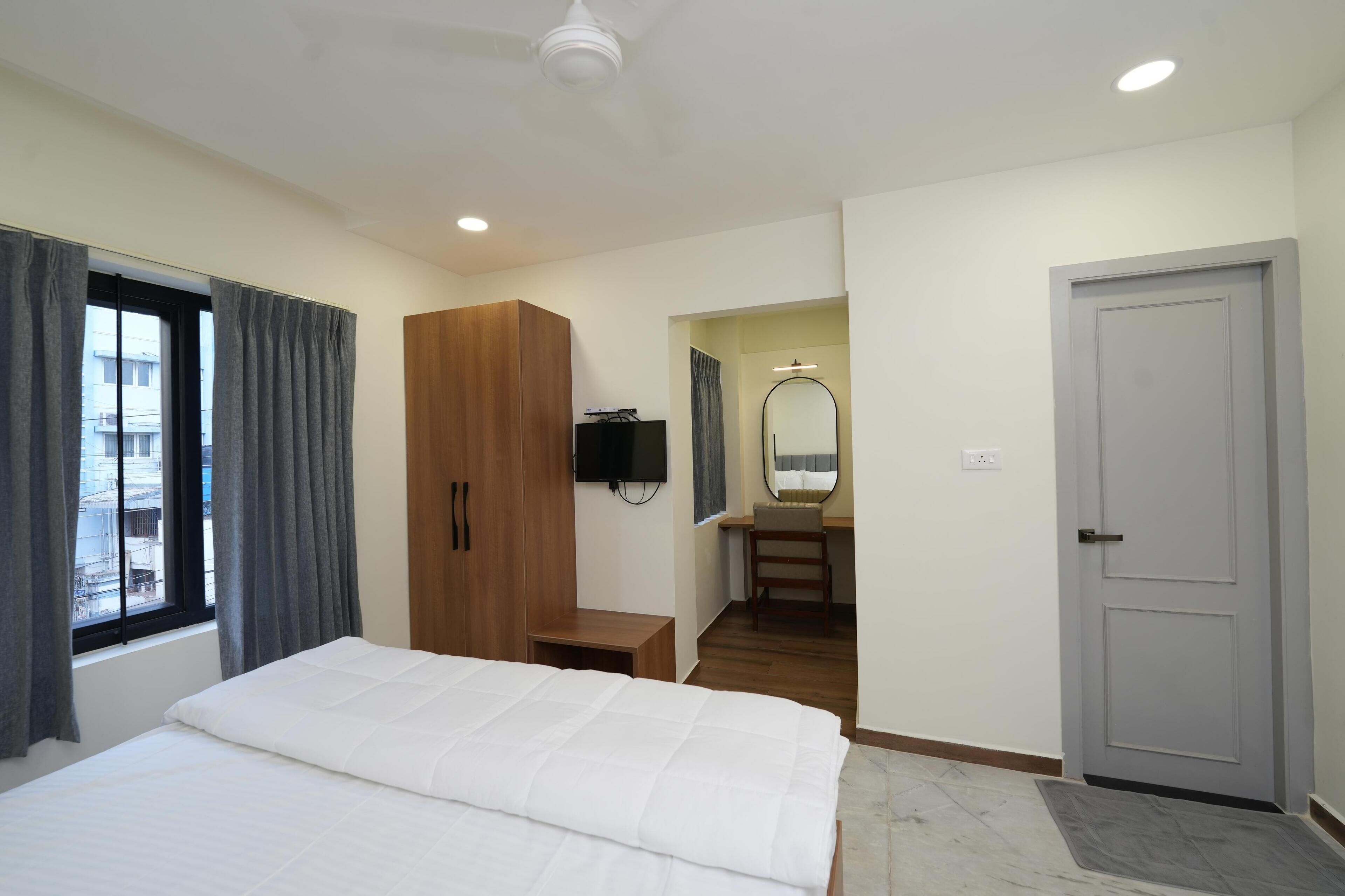 Habitación de hotel con cama, armario, escritorio con silla, espejo y puerta.