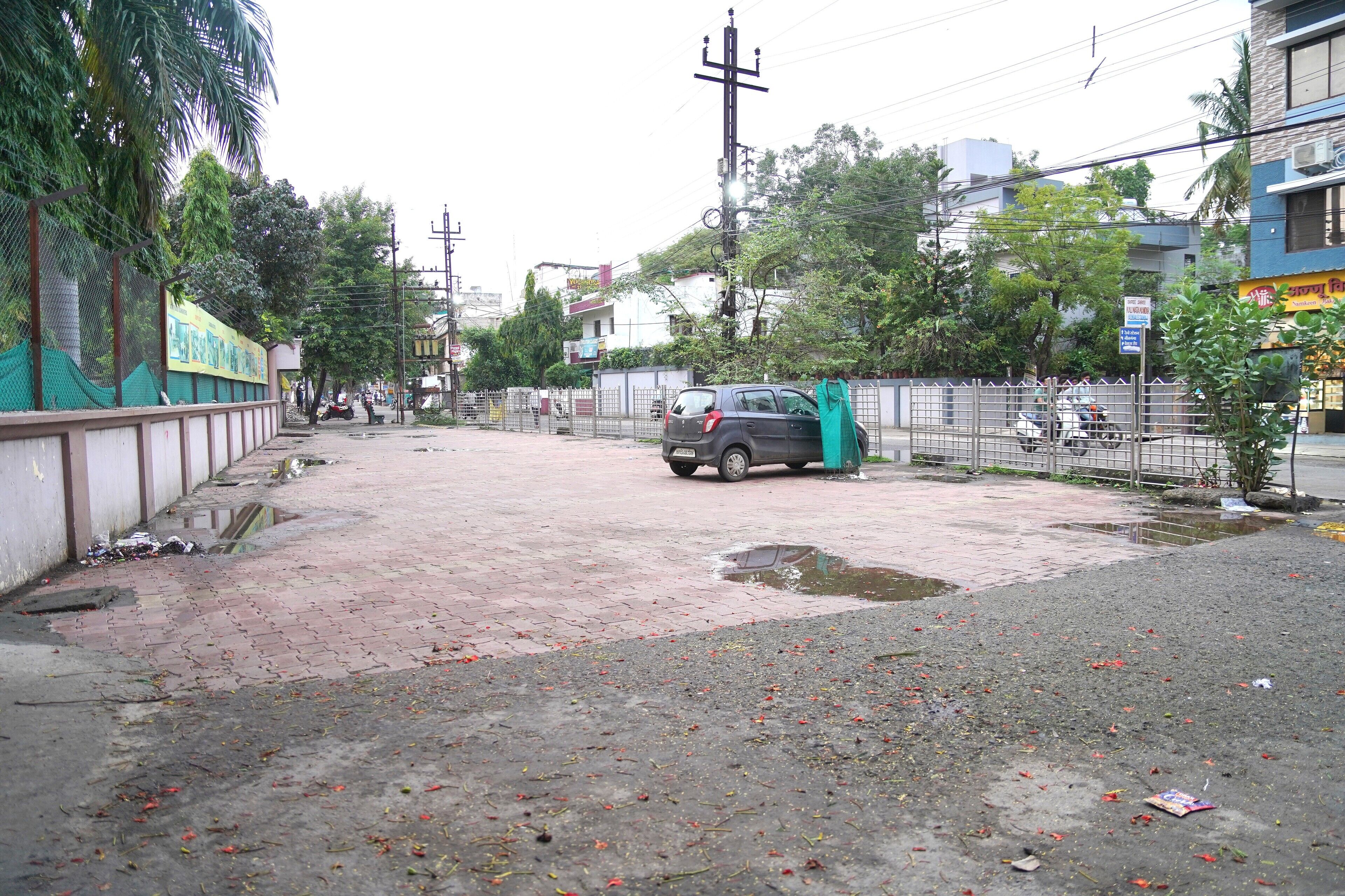 A paved area with a parked car, a fenced playground, and buildings in the background.
