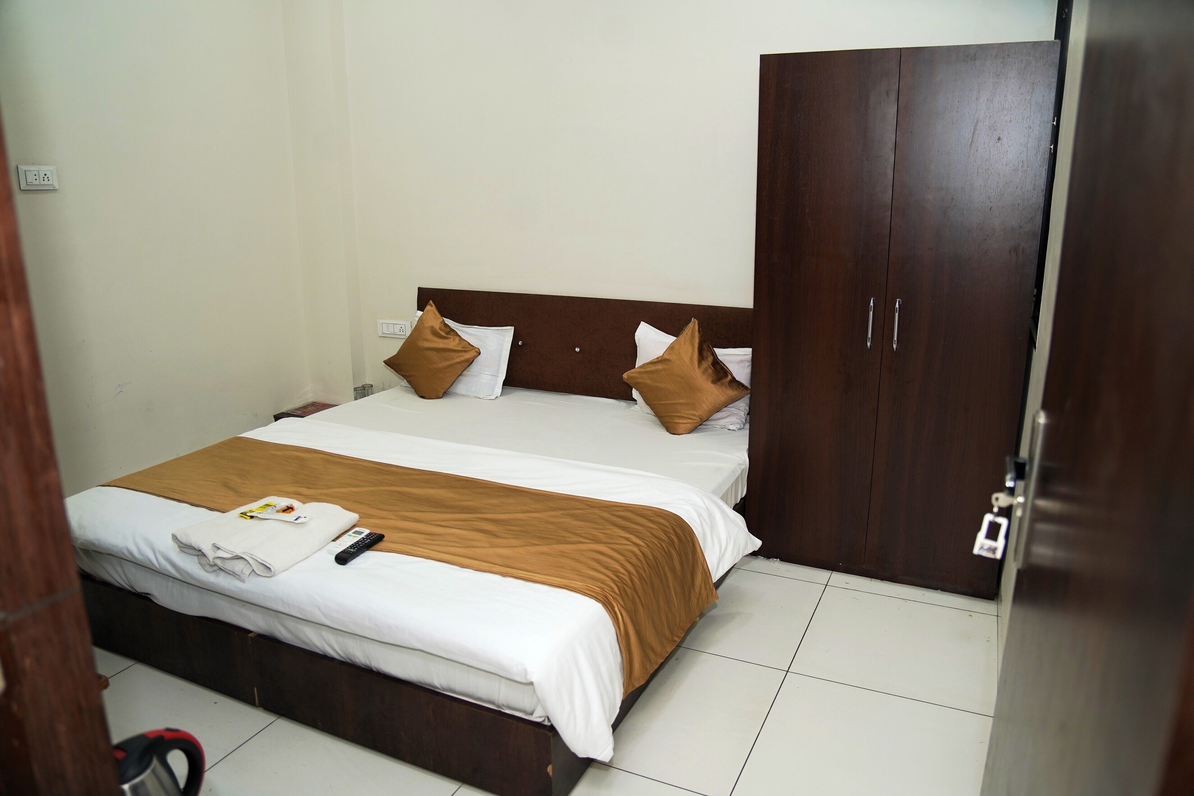 A neatly made bed with white and brown bedding, a remote control, and a folded towel on the bed.