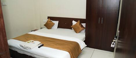 A neatly made bed with white and brown bedding, a remote control, and a folded towel on the bed.