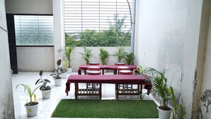 Una habitación con una mesa roja, sillas blancas y plantas en macetas.